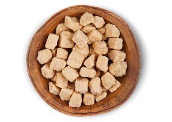 Wooden bowl plate of natural brown unrefined sugar cubes on white background.
