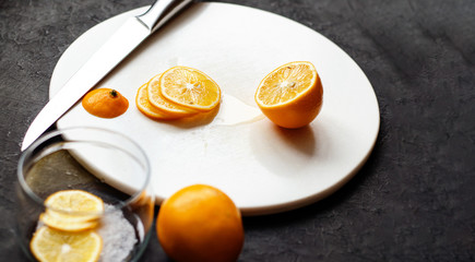 Dark moody. Food black background. On a white stone board in the hands of a girl, a knife cuts a lemon. Slices of lemon are piled in a glass jar and sprinkled with sugar. 