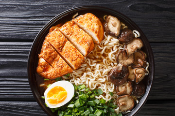 Asian style soup with ramen noodles, chicken, boiled eggs, mushrooms and green onions close-up in a bowl. Horizontal top view
