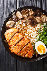 Asian noodle soup with chicken, mushrooms, eggs and herbs close-up in a bowl Vertical top view