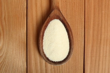 Farina (semolina) on wooden spoon at plank background. Directly Above.
