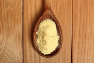 Cornmeal (corn flour) on wooden spoon at plank background. Directly Above.
