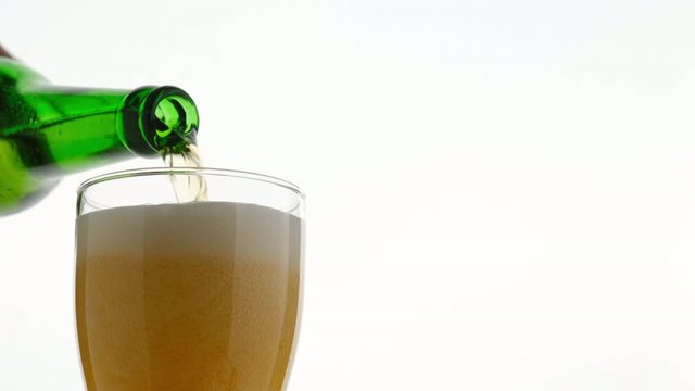 pouring lager beer from green bottle in glass, with bubbles and froth in glass, froth overfill and run out, slow motion. white background