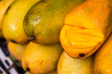 Exotic, tropical fruits on the market, large orange and yellow mangoes on a mango bazaar sliced.