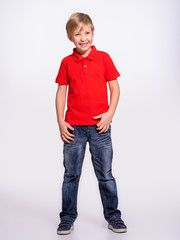 Young pretty boy posing at studio as a fashion model. Photo of a 8 years old kid. Full portrait of happy boy, isolated.  Portrait of white smiling kid in a red t-shirt and jeans. Boy in a full length © Valua Vitaly