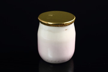 Yogurt in small glass jar with aluminium foil seal cap at black