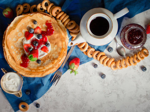 Overhead stack of thin pancakes poured with sour cream and decorated with fresh strawberries and blueberries. The concept of Russian tea party at holiday Maslenitsa, Shrovetide