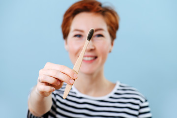 Cheerful woman with short ginger hair showing a wooden toothbrush