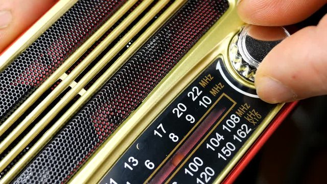 Human hands with fingers adjusts the tuning old radio to radio wave. Turns knob in search of interesting radio station. Close-up.