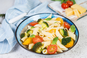 Boiled Penne with vegetables, broccoli, tomatoes and fresh herbs. Close-up, selective focus.