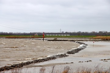 Water blown over lines of stone at river Hollandsche IJssel at Nieuwerkerk in the Netherlands - obrazy, fototapety, plakaty