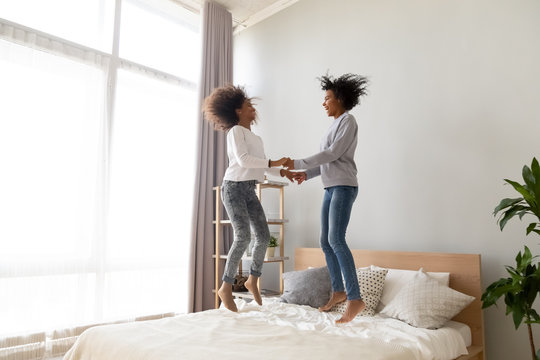 Happy African Mom And Cute Teen Daughter Jumping On Bed