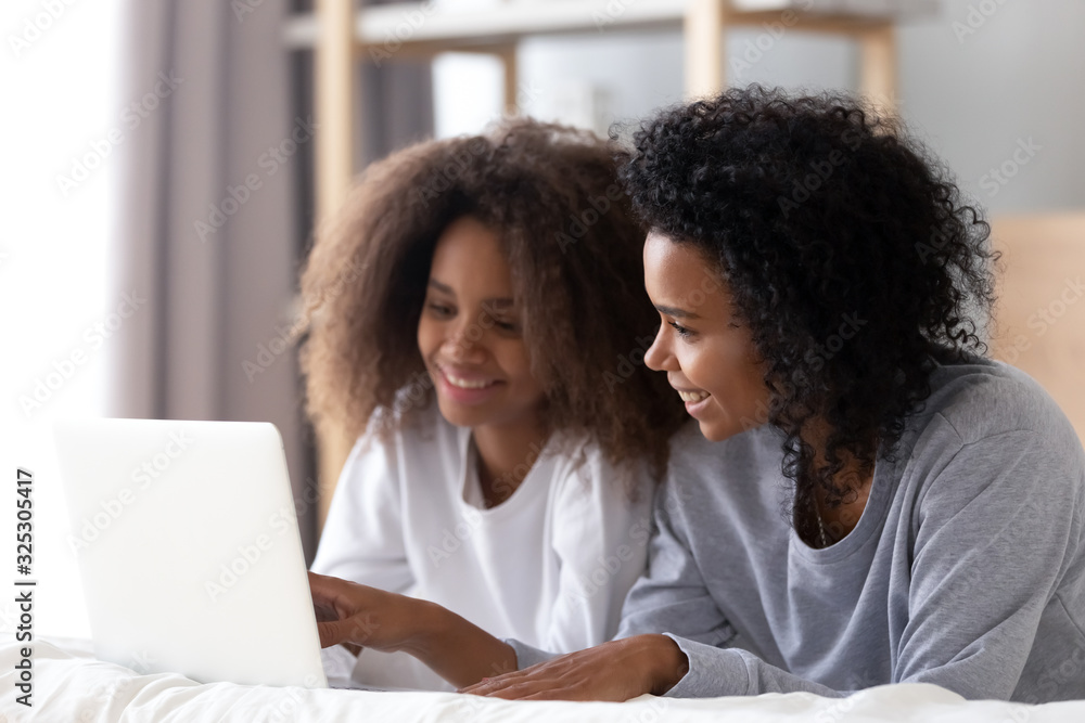 Wall mural african mom and teen daughter using laptop lying on bed