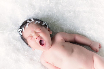 Cute baby on newborn is yawning on a white fluffy fur. Fashion baby portrait concept.