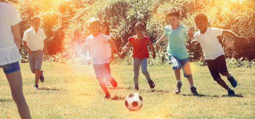 Obraz na płótnie Canvas Company of glad children playing football on the playground in park