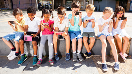 Children using mobile devices  outdoors at sunny day