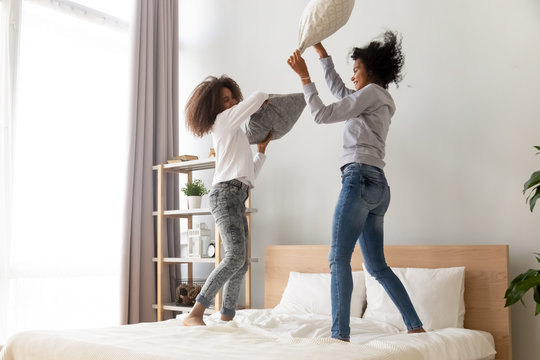 Happy African Mom And Teen Having Pillow Fight On Bed