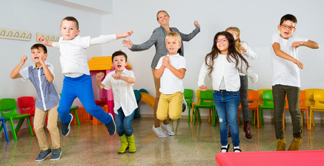 Obraz premium Positive female teacher and group of schoolkids jumping in classroom