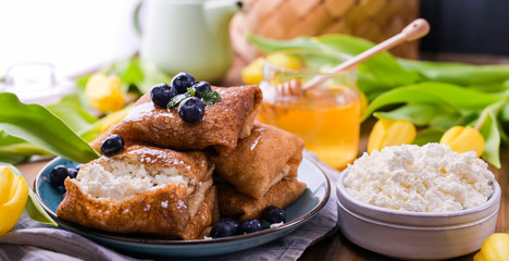 Large traditional Russian pancakes with berries and honey on a wooden table. Baking for the spring holiday Shrovetide and a bouquet of yellow tulips. Copy space