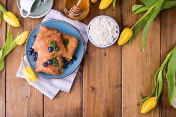 Large traditional Russian pancakes with berries and honey on a wooden table. Baking for the spring holiday Shrovetide and a bouquet of yellow tulips. Copy space