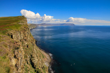 Die Landschaft einer kargen Steilküste im Norden von Island in den Westfjorden vor weitem blauen Meer mit blauem Himmel und Wolken mit Blick über die Küste