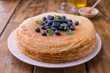 Pancakes with blueberries and honey on a plate, on wooden roofing. Traditional pastries for the Russian festival of Maslenitsa. free space for text.