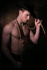 Handsome cowboy wearing a hat with barechest showing defined pecs and sixpack abs, muscular arms holding onto rope