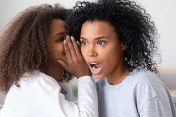 Fototapeta na wymiar African american teen daughter whispering in mom ear telling secret