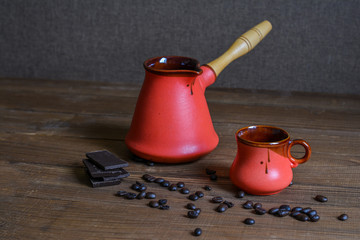 Ceramic cup, coffee cezve, coffee grains, wooden background and pieces of chocolate