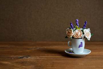 Bouquet in a cup on a wooden table and a dark background. Beautiful little flowers in a white cup with place for text.