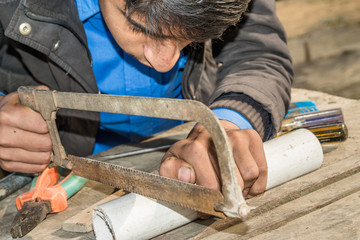 a teenage is cutting PVC pipe with saw 