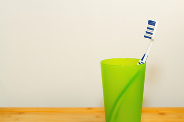 Eine Zahnbürste steht in einem hell grünen Plastik Becher vor weißem Hintergrund