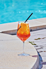 Wine Glass of cold cocktail Aperol spritz against turquoise water of poolside. Traditional Italian...