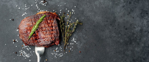 grilled beef steak on a fork with spices on a stone background with copy space for your text