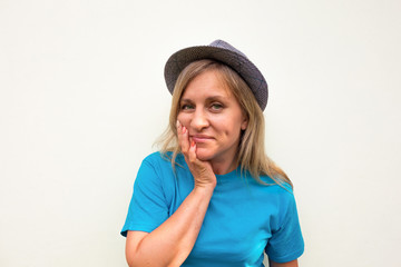 Woman in hat. White girl looks at camera, smiles and touches her cheeks with hand. Front portrait with positive face and long hair