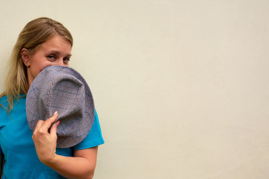 Woman covers her face with hat. White long hair girl looks at camera and shy or flirt making eyes at you. Front portrait with happy face. Copy space is available