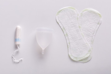 Two women's white hygiene pads, menstrual cup and tampons isolated over light background. Hygiene, ginecology, intimate concept, best methods of hygiene for women. Critical days, menstruation.
