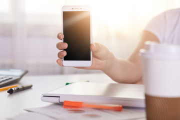 Close up portrait of unknown woman hand presenting smartphone with empty black screen for montage your texts or pictures, lady holds mobile phones with workspace on blurred background. Technology.