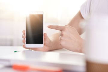 Picture of unknown woman holding mobile phone with isolated display, gadget with blank black screen, faceless female pointing at device with her index finger. Copy space for advertisment or promotion.