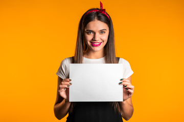 Pretty asian girl holding white a4 paper poster. Copy space. Smiling trendy woman with long hair on studio background.