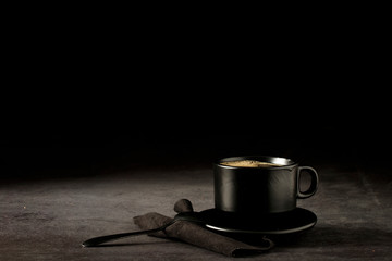 Black coffee cup with coffee on a dark background. With copy space for your text. Cup of coffee on a black background low key copy space.