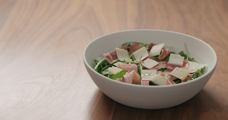 salad with arugula, prosciutto and cherry tomatoes in white bowl on walnut table