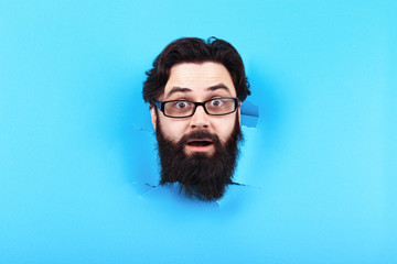 surprised bearded man in hole in the blue background