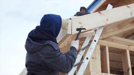 View from below of worker fixing plank with nails during assembling wooden trussing for small roof above the porch. Frame house building - Powered by Adobe