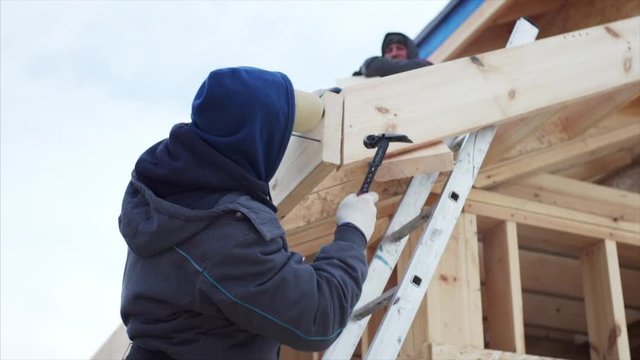 View from below of worker fixing plank with nails during assembling wooden trussing for small roof above the porch. Frame house building