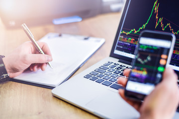 Modern laptop with financial bitcoin cryptocurrency crypto graph data trade on notebook screen. Computer workplace detail on table. Business man using pen indicates in the graphics.