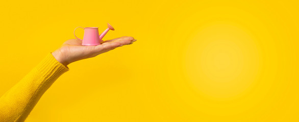 pink mini watering can on hand over yellow background, panoramic mock-up
