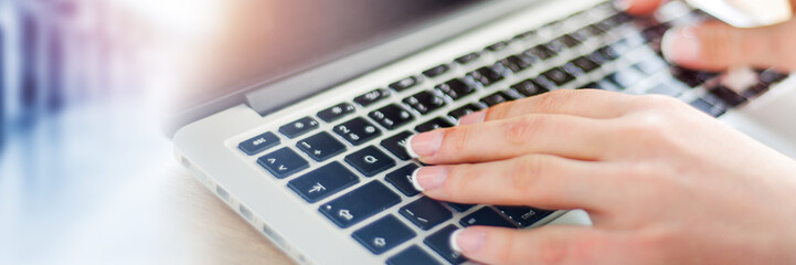 Woman working in office with laptop writing a blog. Female hands on the keyboard banner or panorama.
