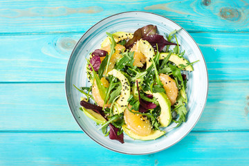 Vegan grapefruit, avocado and arugula salad on blue wooden background.