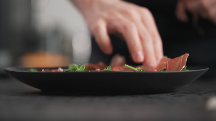 prosciutto falling into black plate with arugula leaves